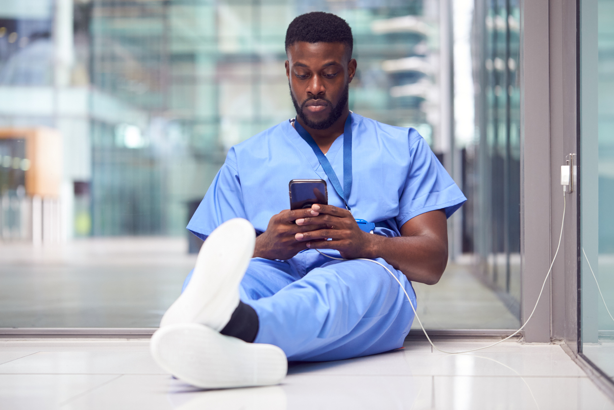 Enfermeiro sentado no chão e mexendo no celular