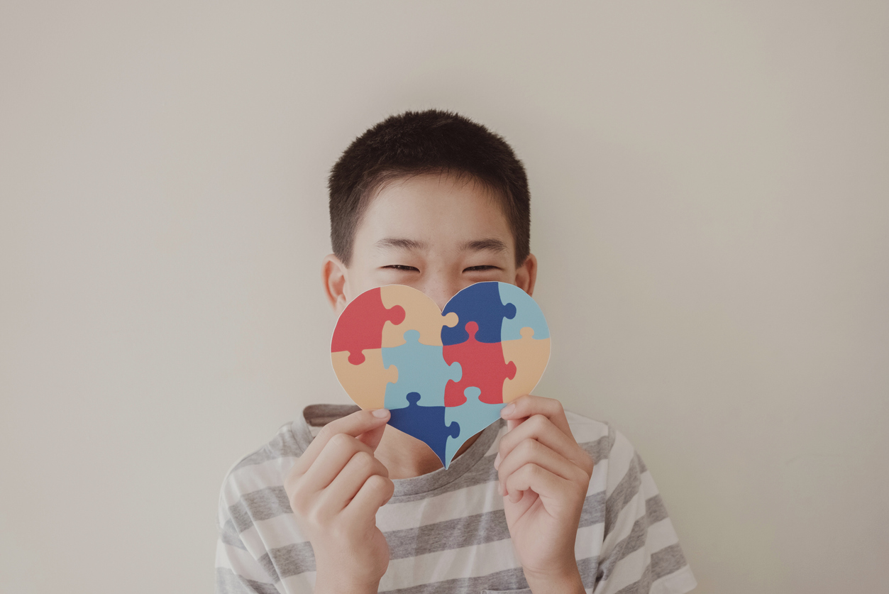 Menino segurando um coração feito de quebra-cabeças símbolo do autismo