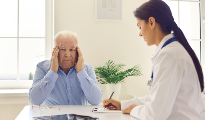 Cefaleia em salvas: homem idoso com dor de cabeça dentro de um consultório acompanhado por uma médica