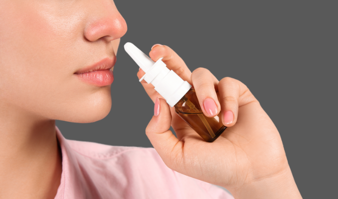 Top 5 notícias: mulher jovem aproximando um spray nasal de seu próprio nariz