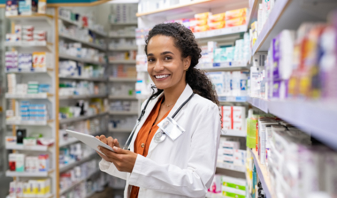 Top 5 artigos 2023: farmacêutica segurando um remédio com as prateleiras de medicamentos ao fundo