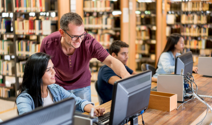 Bibliotecário ajudando alunos em uma pesquisa no computador de uma biblioteca