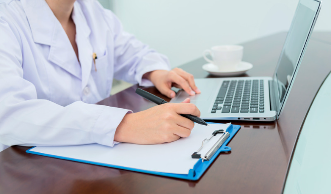 Interoperabilidade: médico usando um notebook enquanto verifica o prontuário físico de um paciente