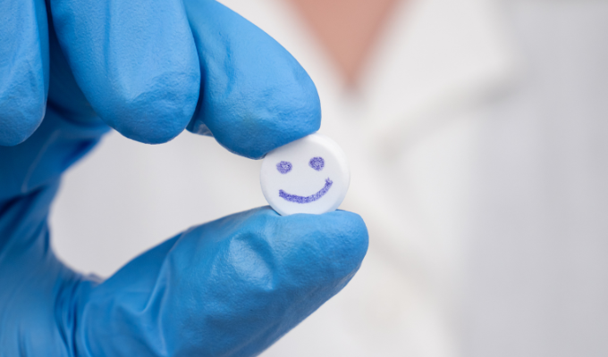 Psicoativos: cientista segurando um comprimido com um rosto feliz desenhado que representa a substância psicoativa